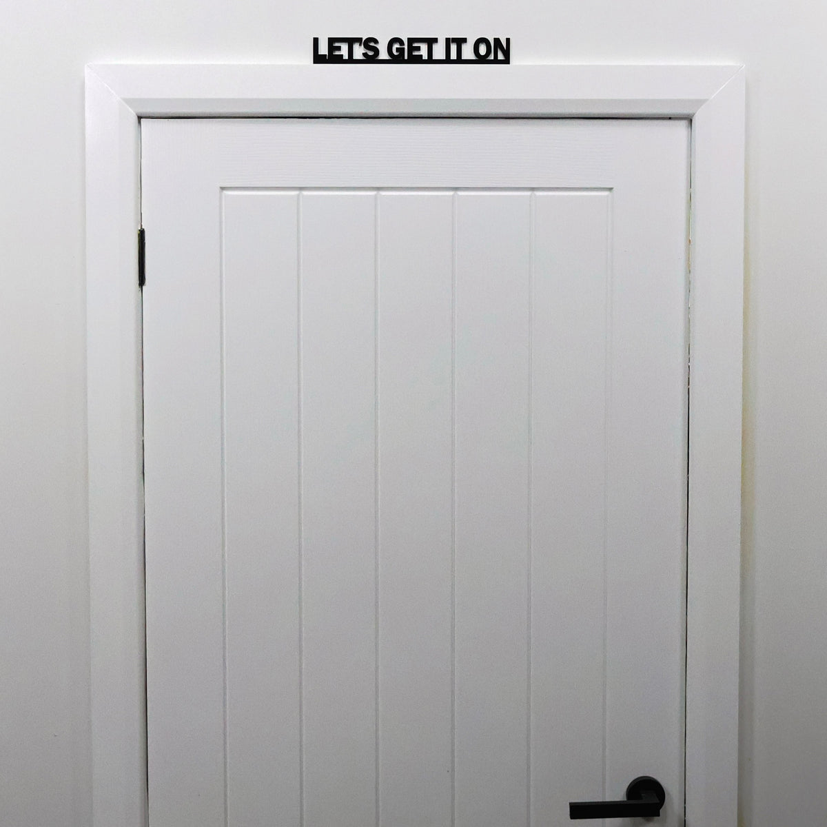 Humorous black acrylic Door Topper shown from a distance on a door frame in a modern bedroom.
