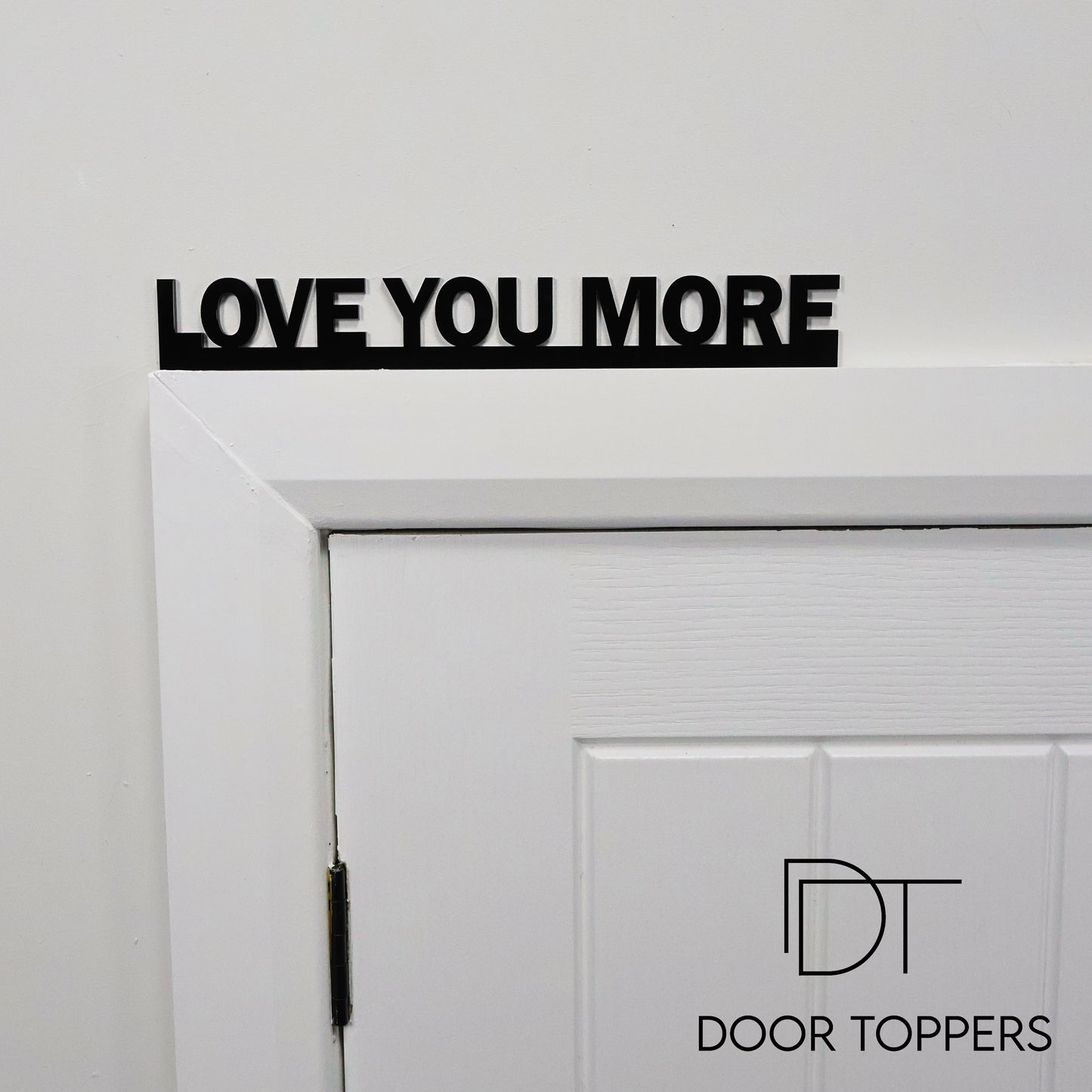 LOVE YOU MORE black acrylic Door Topper sign displayed above a white door frame in a modern home
