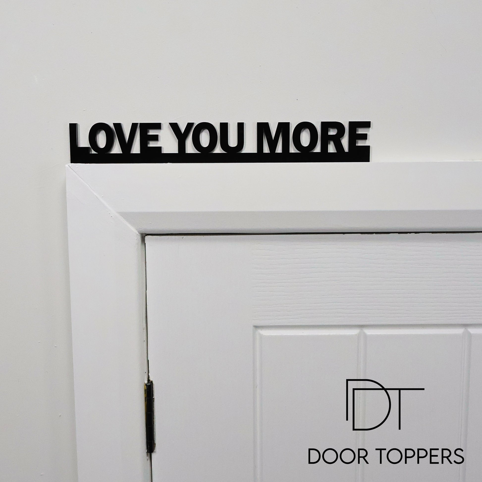 LOVE YOU MORE black acrylic Door Topper sign displayed above a white door frame in a modern home