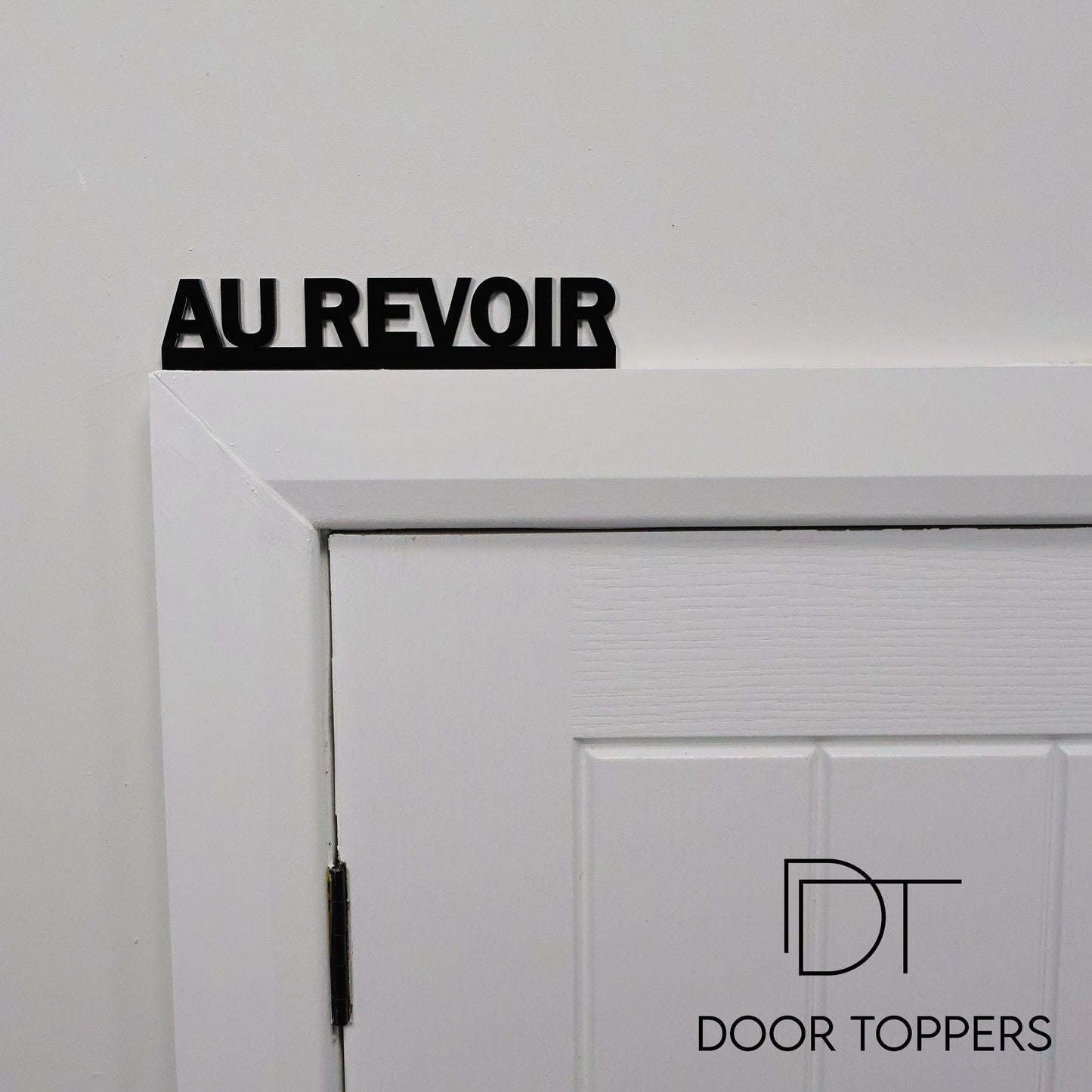 AU REVOIR black acrylic Door Topper displayed above a hallway door in a modern home.