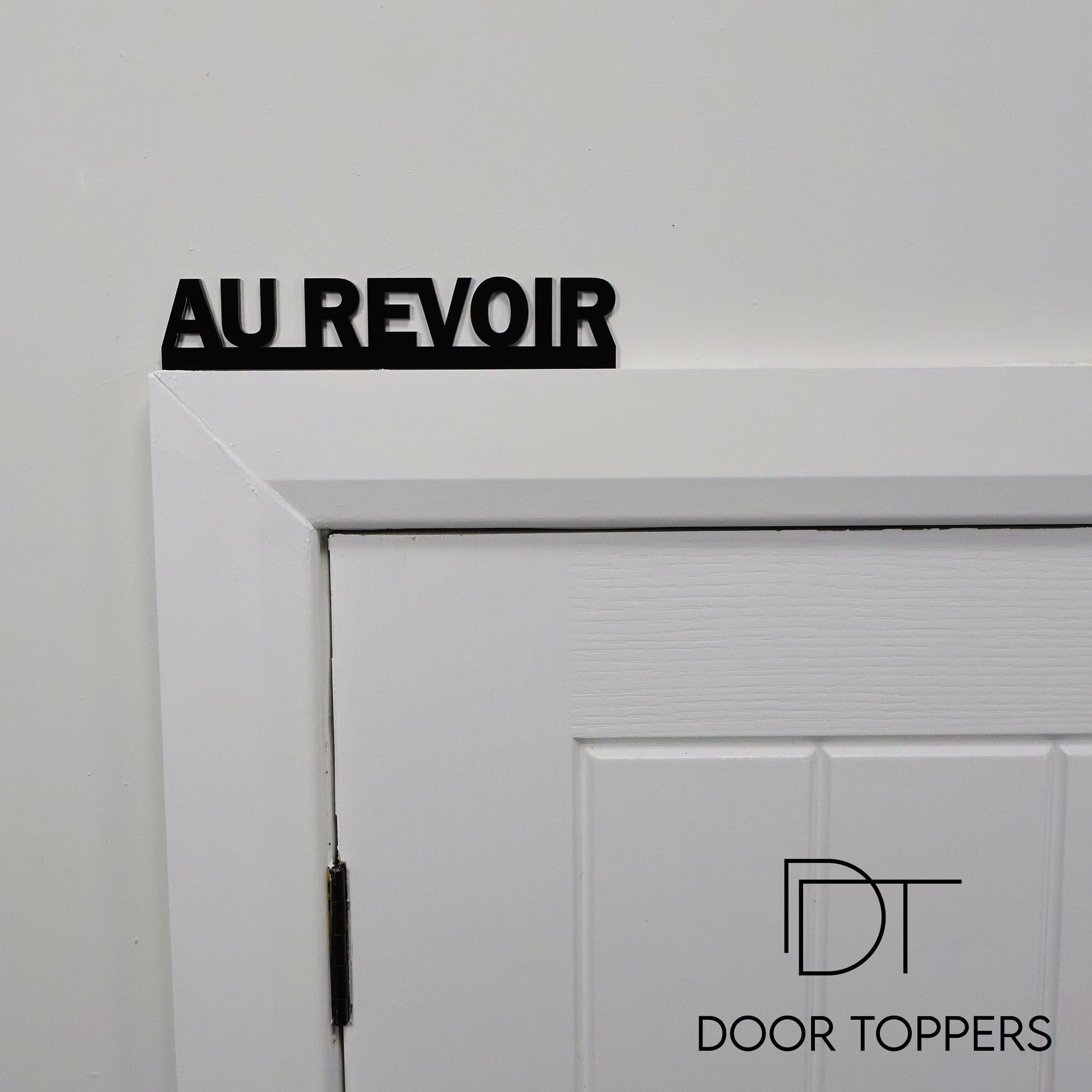 AU REVOIR black acrylic Door Topper displayed above a hallway door in a modern home.