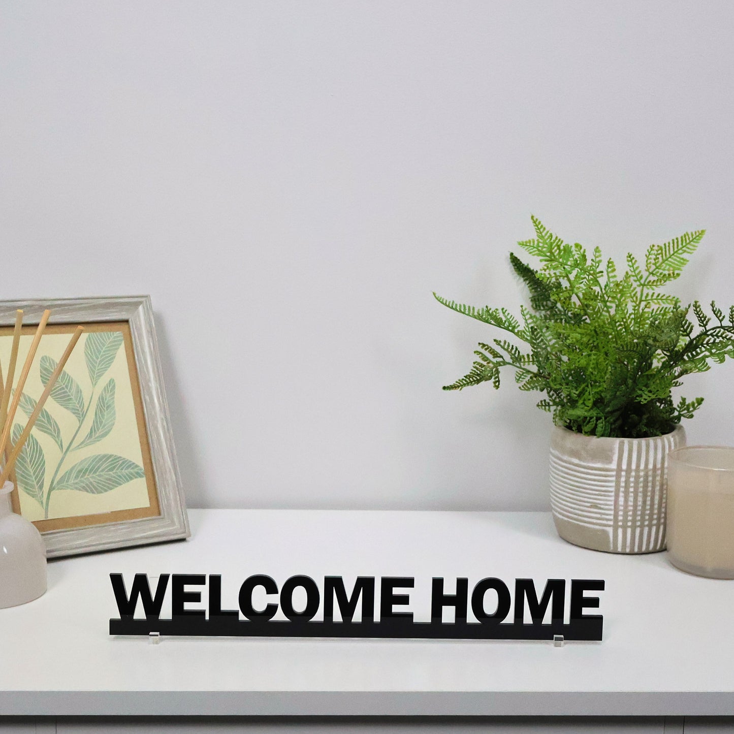 Black acrylic WELCOME HOME Door Topper shown freestanding on shelf