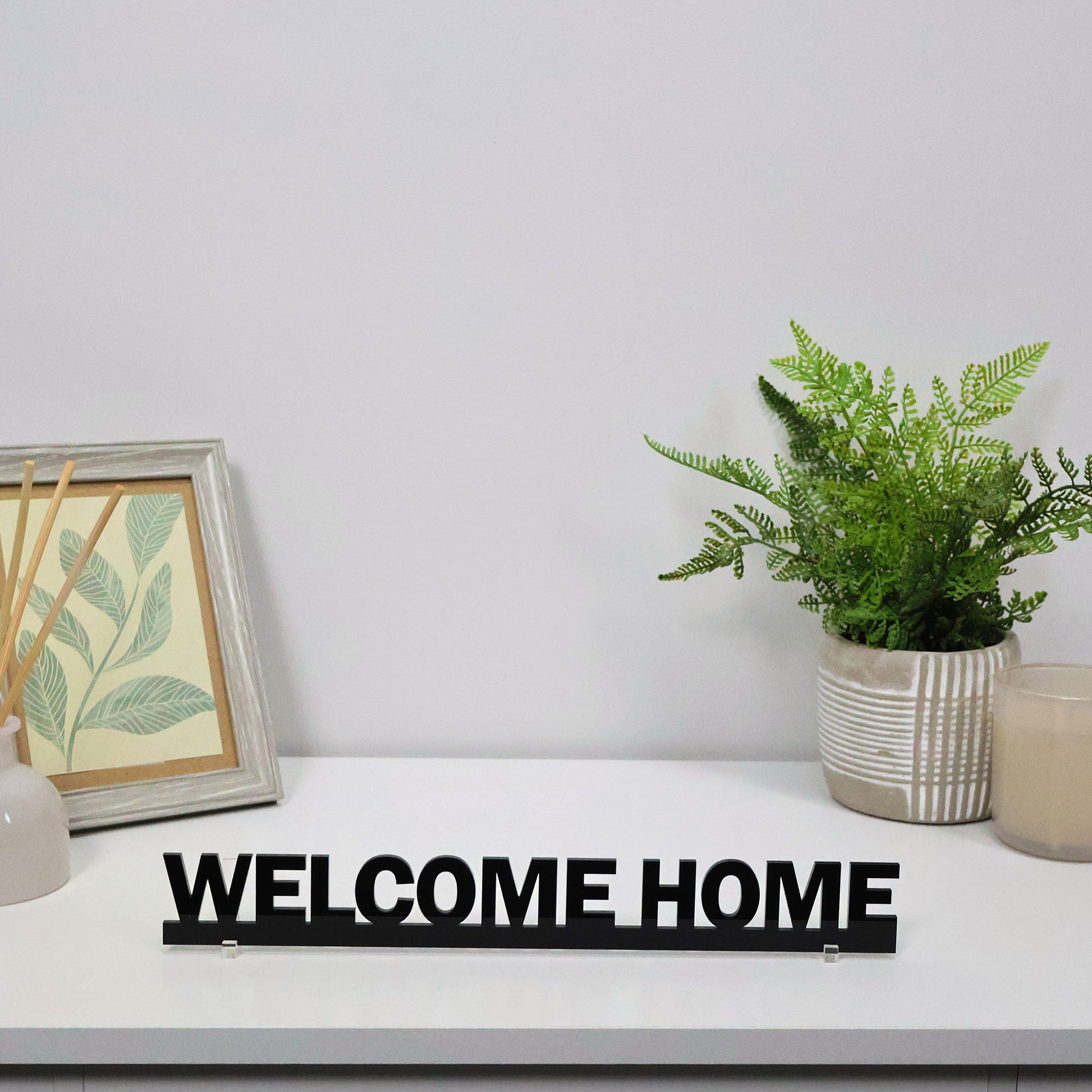 Black acrylic WELCOME HOME Door Topper shown freestanding on shelf