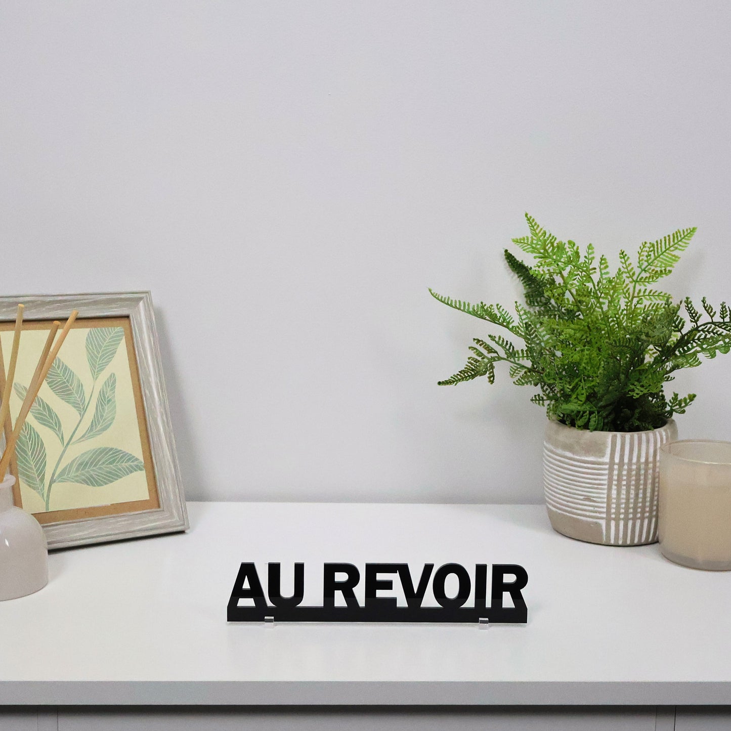 AU REVOIR Door Topper freestanding on a console shelf beside candles and books.