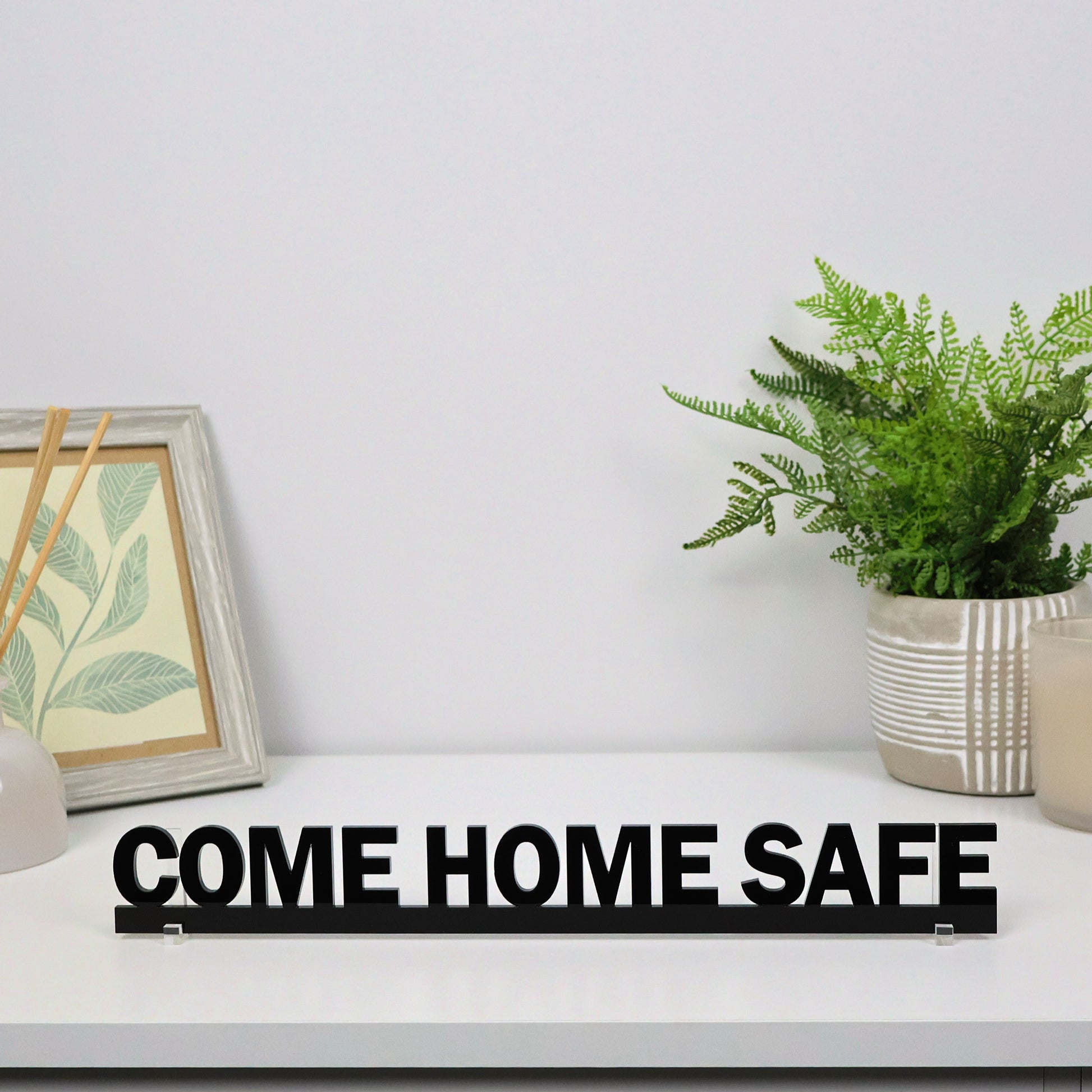 COME HOME SAFE Door Topper freestanding on a shelf beside books