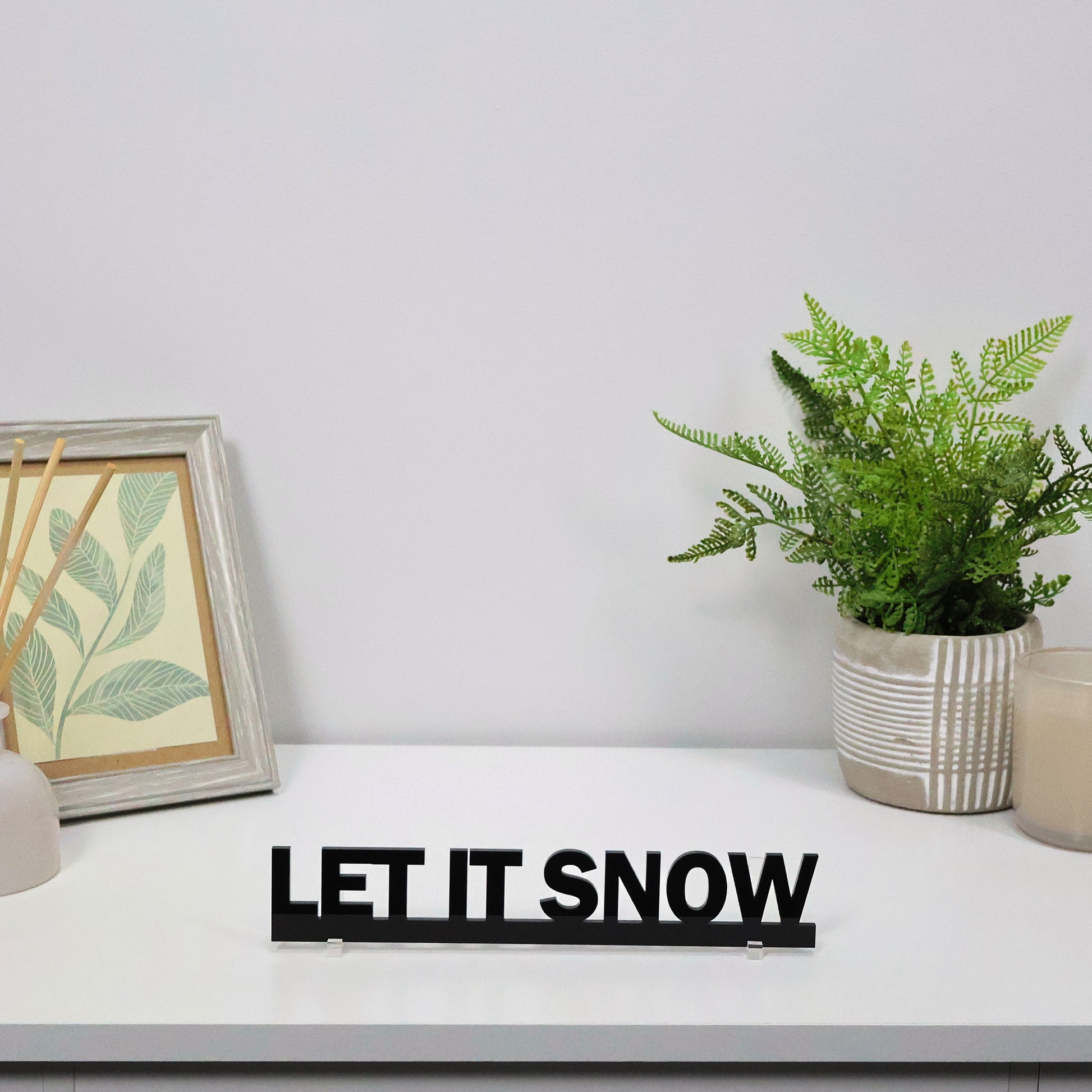 LET IT SNOW sign shown freestanding on a mantel beside fairy lights
