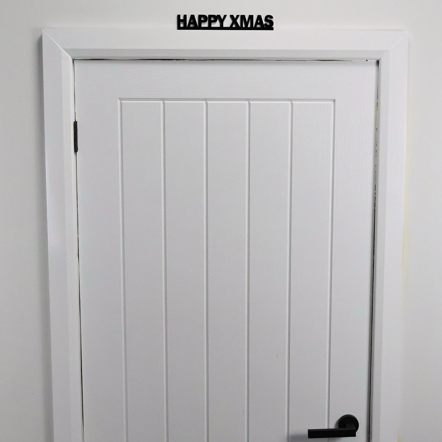 Black recycled acrylic festive sign styled on a shelf with tinsel and fairy lights.