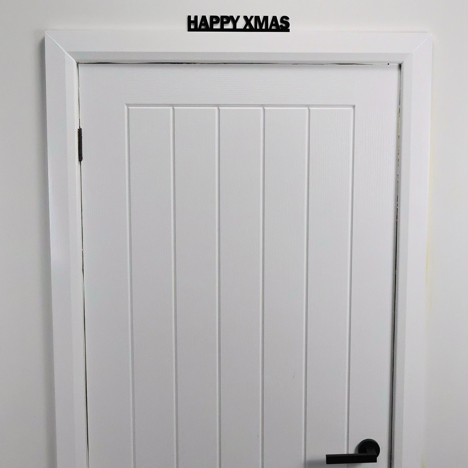 Black recycled acrylic festive sign styled on a shelf with tinsel and fairy lights.