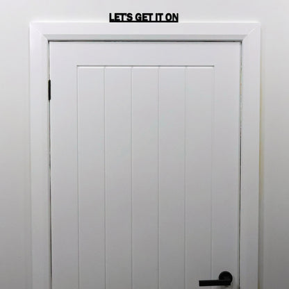 Humorous black acrylic Door Topper shown from a distance on a door frame in a modern bedroom.