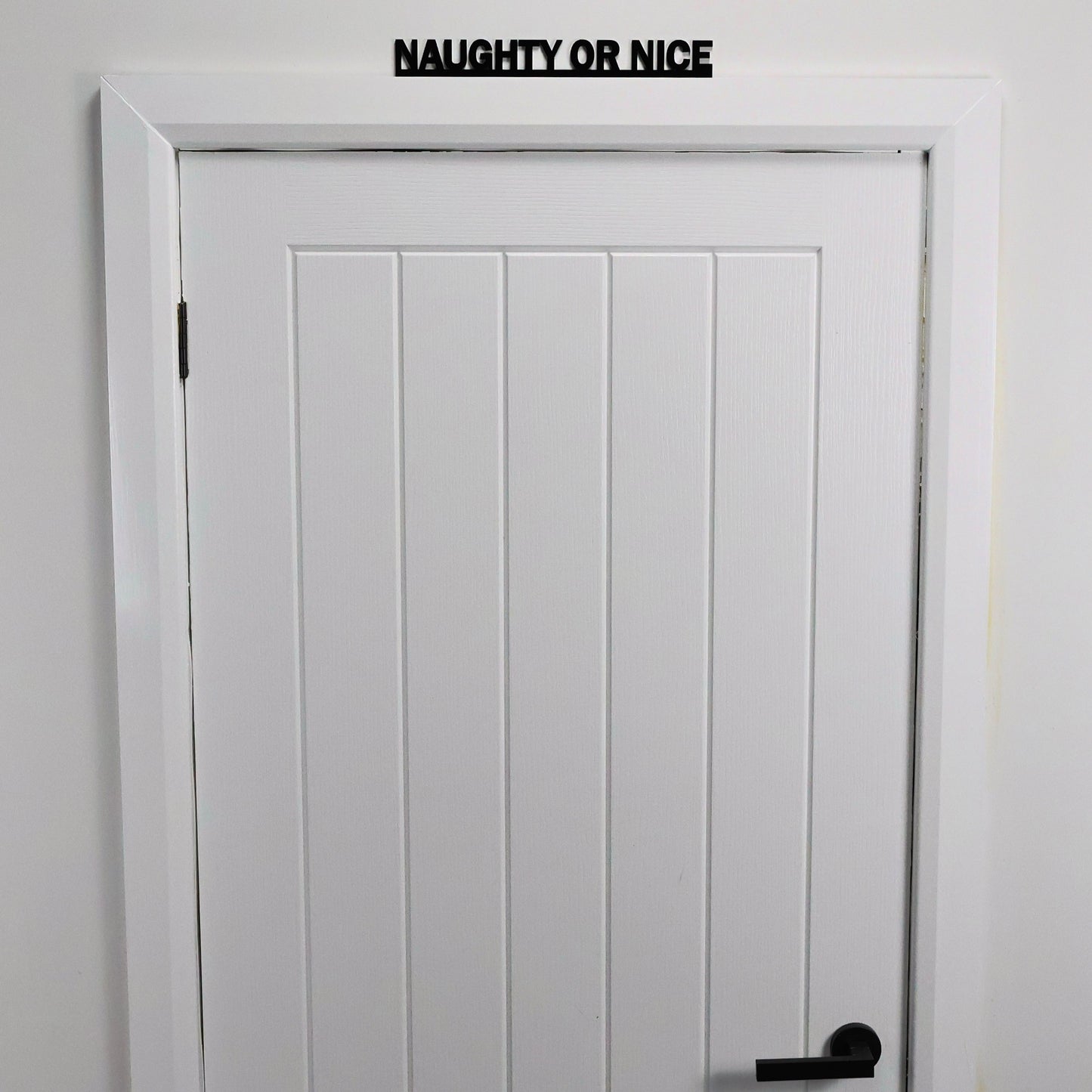 Black recycled acrylic festive sign styled on a shelf with fairy lights and garlands.