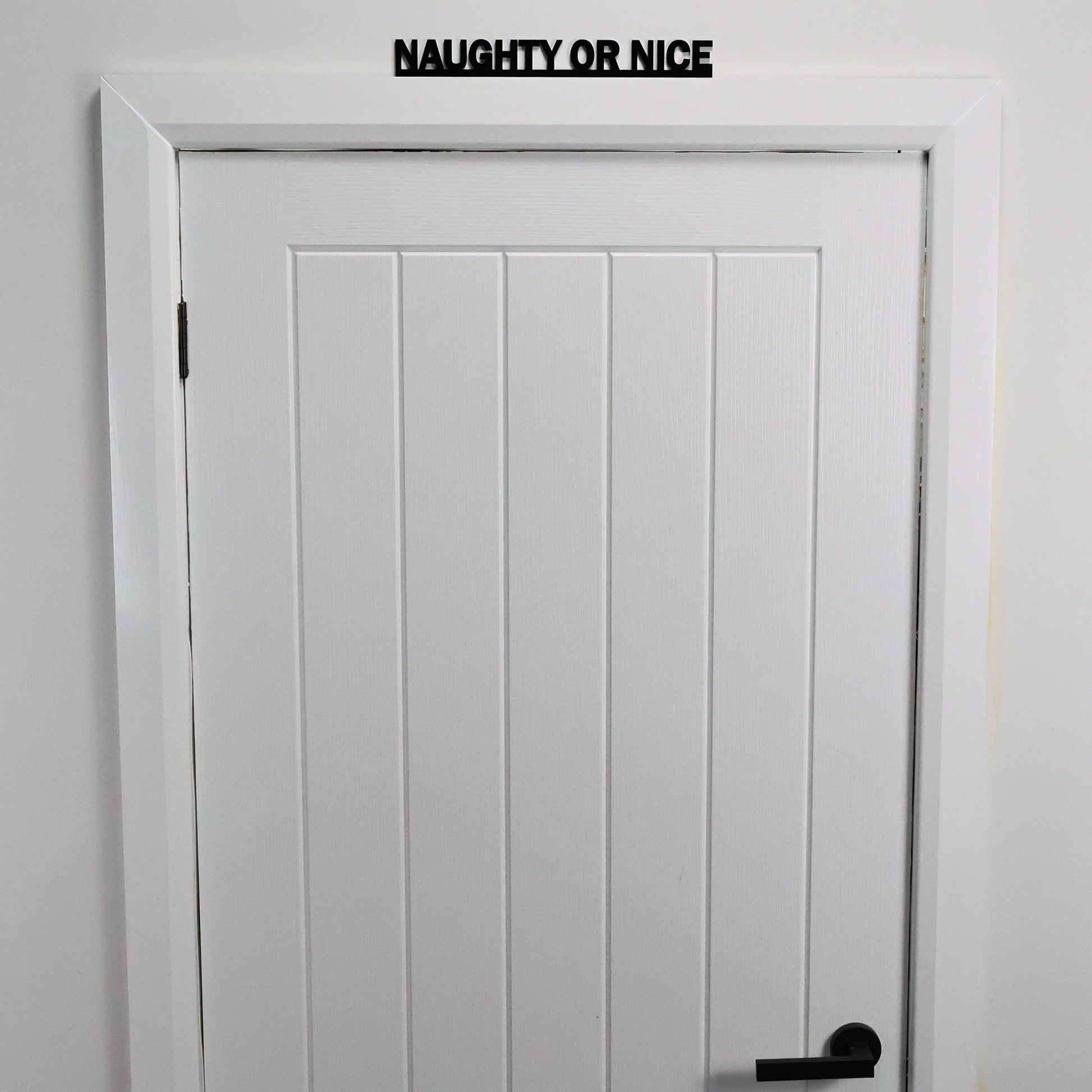 Black recycled acrylic festive sign styled on a shelf with fairy lights and garlands.