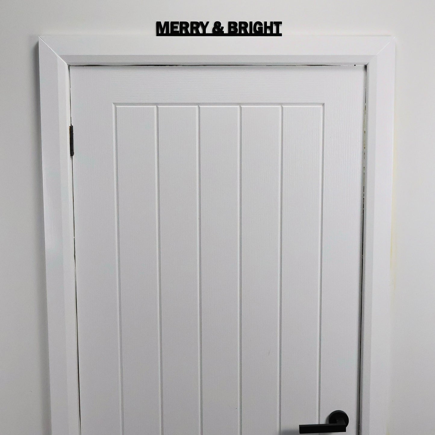 Black acrylic festive wall sign displayed above a white door frame