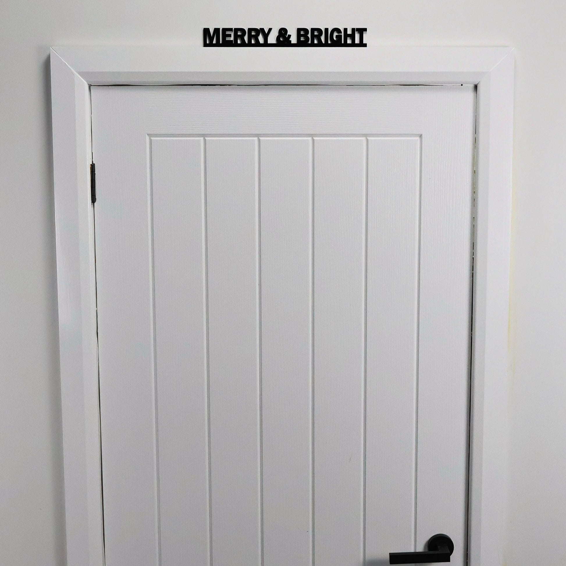 Black acrylic festive wall sign displayed above a white door frame