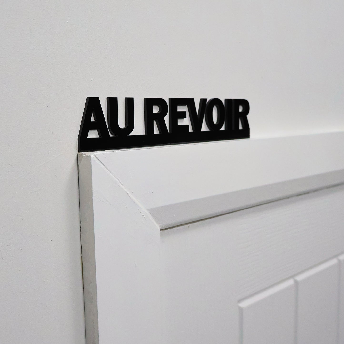 Close-up of glossy black lettering on the AU REVOIR wall sign.