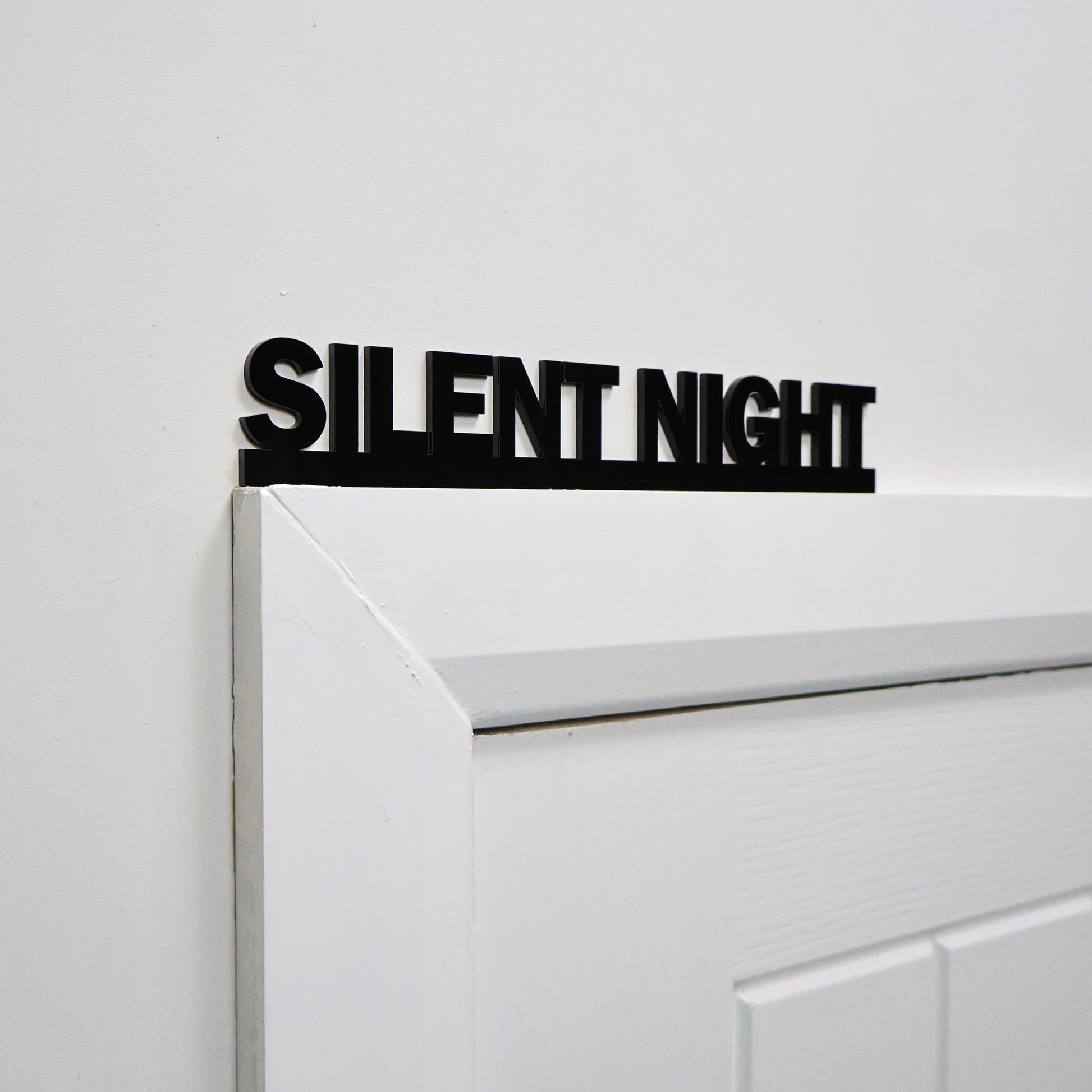 Black acrylic festive wall sign displayed above a white door frame