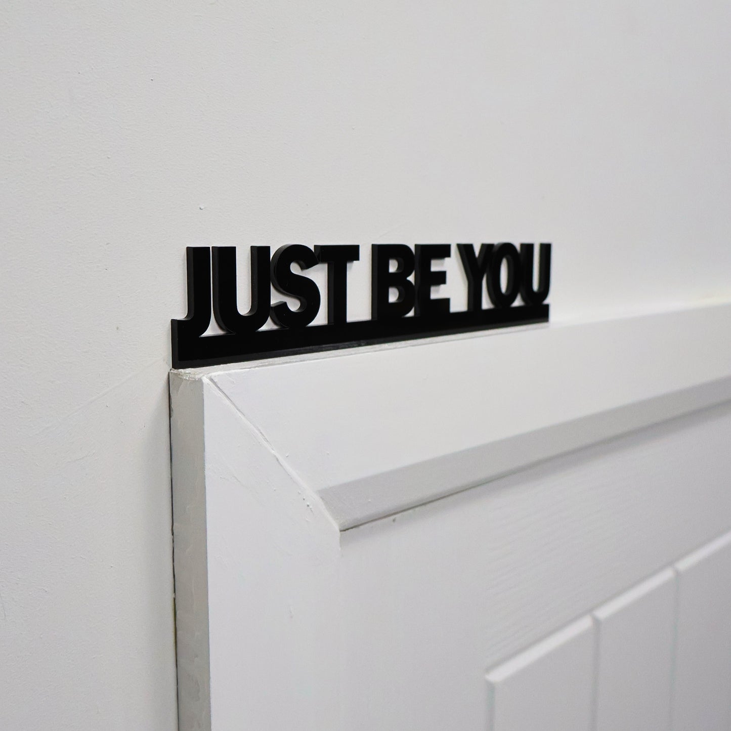 Uplifting black wall sign displayed above a standard white door frame
