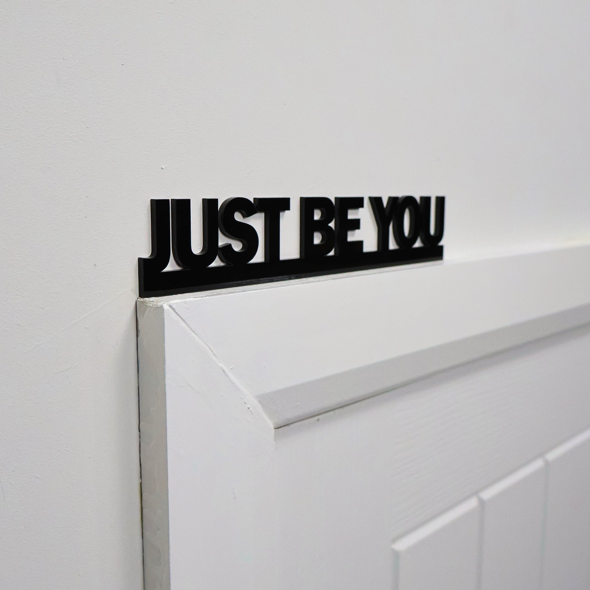 Uplifting black wall sign displayed above a standard white door frame
