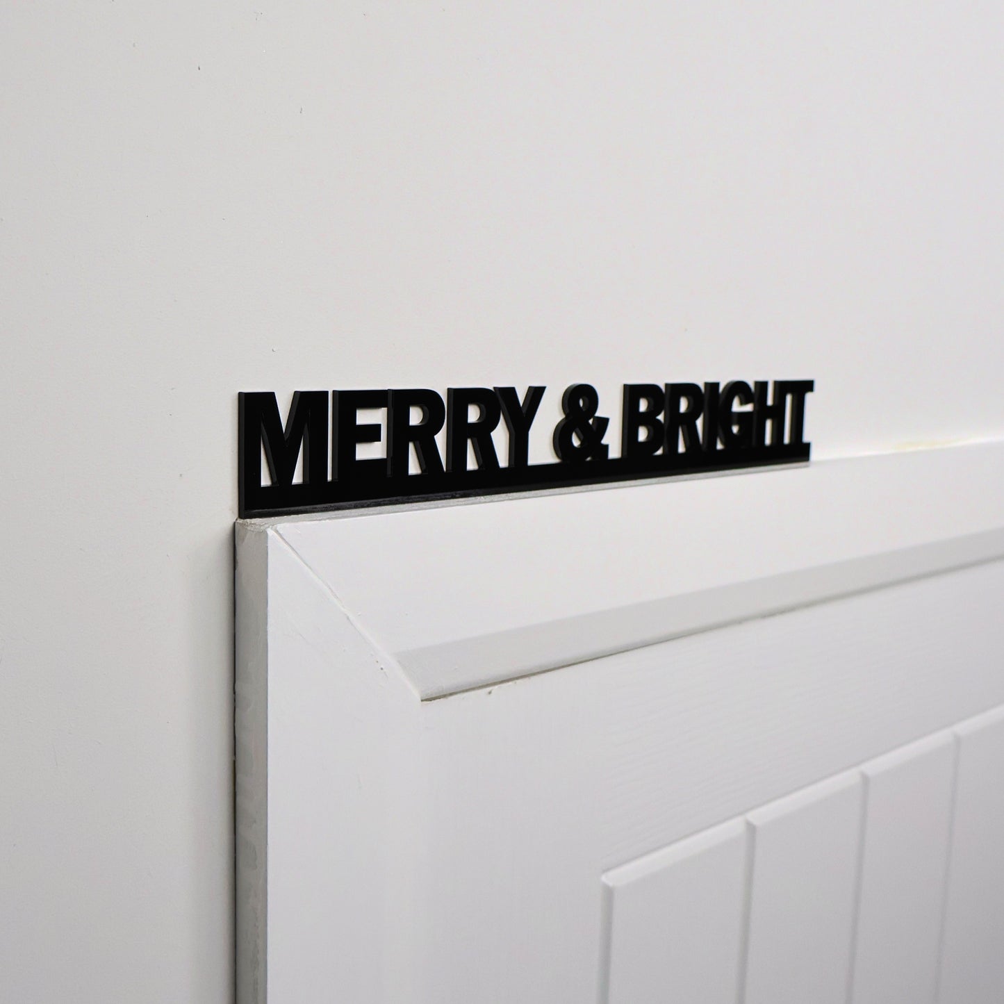 Black acrylic MERRY & BRIGHT sign shown above a door frame