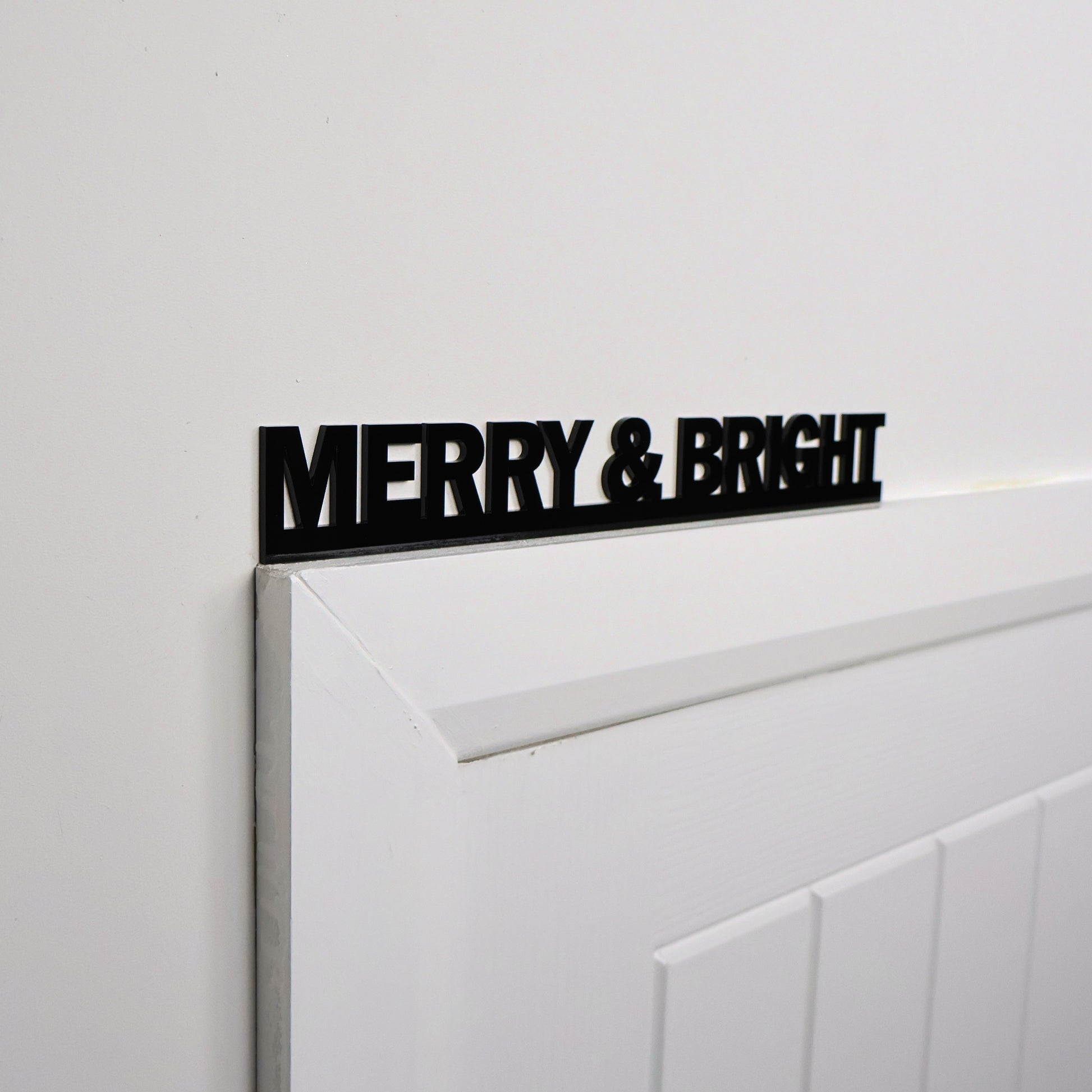 Black acrylic MERRY & BRIGHT sign shown above a door frame