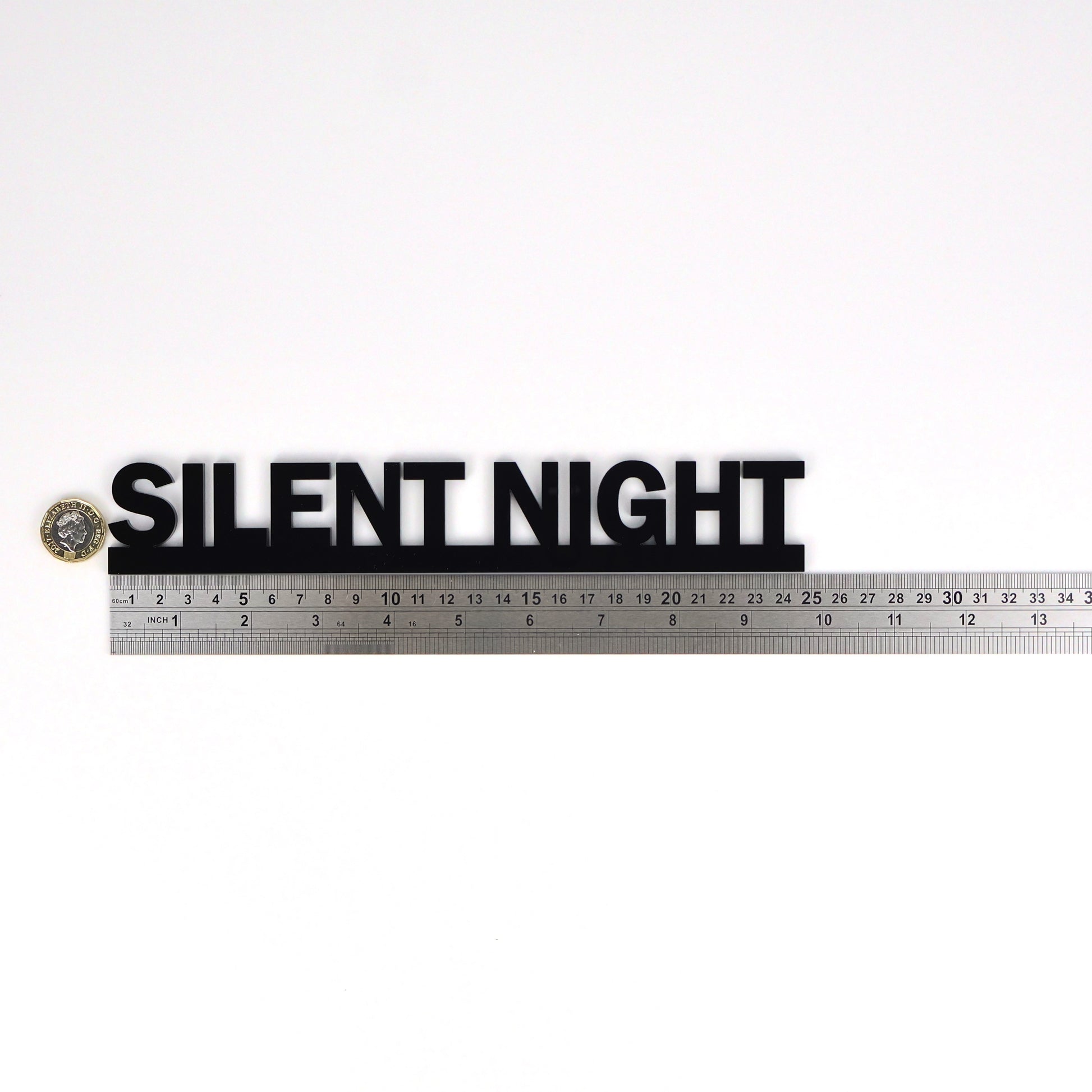 Black acrylic SILENT NIGHT Door Topper shown beside a ruler and pound coin for scale